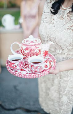 a woman holding a tray with two tea cups and saucers on top of it