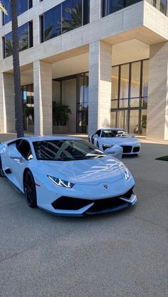 two blue sports cars are parked in front of a large building with palm trees on the sidewalk