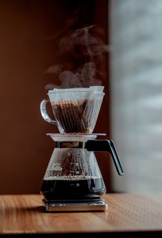 a coffee maker with steam coming out of it's filterr on a wooden table