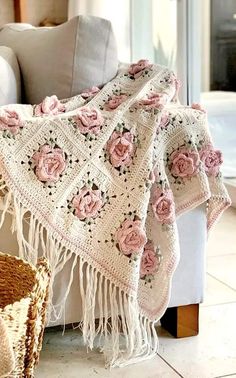 a crocheted blanket with pink roses on it sitting on a couch next to a basket