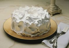 a white frosted cake sitting on top of a wooden plate next to silverware