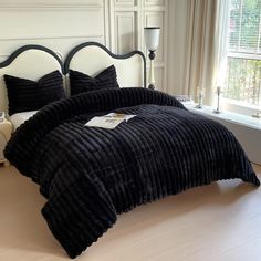 a bed with black bedspread and pillows in front of a window