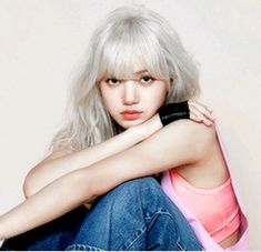 a woman with white hair sitting on the floor next to a wall and holding a cell phone