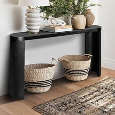 two baskets sitting on top of a wooden table next to a lamp and rug in a room