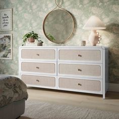 a white dresser sitting next to a bed in a room with green wallpaper and a round mirror on the wall