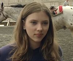 a young woman is standing in front of two horses and looking at the camera with an intense look on her face