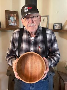 an old man holding a wooden bowl in his hands and wearing a hat on top