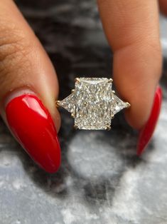 a woman's hand with red nails and a ring on her finger that has a diamond in it