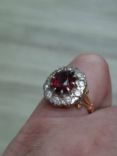 "A vintage 18ct gold garnet and diamond ring. The ring is not Hallmarked, but is stamped \"18CT.\" The large oval cut garnet is claw set at the centre of the ring and measures 10 x 8mm's. This is then surrounded by ten round brilliant cut diamonds. The total approximate combined weight of these diamonds is 1.00ct, and in our opinion they are a colour G/H with a clarity of SI1. The shoulders are beautifully detailed with a fleur-de-lis on each one, and there is a very intricate design to the sett Luxury Garnet Jewelry With Intricate Design, Luxury Vintage Garnet Rings, Red Garnet Ring 1stdibs, Victorian Garnet Gemstone Rings, Luxury Antique Garnet Rings, Garnet And Diamond Ring, Red Stone Ring, Red Garnet Ring, Amethyst And Diamond Ring