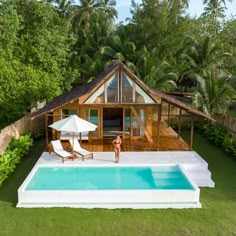 a woman standing next to a swimming pool in front of a wooden structure with an open roof