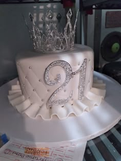 a two tiered white cake with a crown on top is sitting on a table