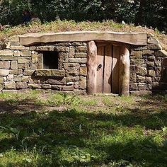 an old stone building with grass growing on the roof and door, in front of some trees