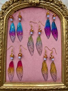 a gold frame with six different colored butterfly wings hanging from it's sides and dangling from earrings