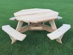 a wooden picnic table sitting on top of a green grass covered field with two benches