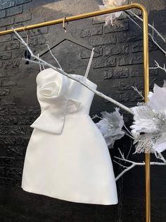 a white dress hanging on a clothes rack with flowers and branches in front of a brick wall