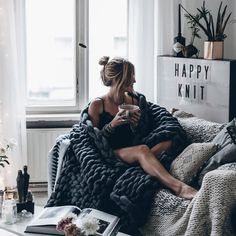 a woman wrapped in a blanket sitting on a couch next to a coffee table and window