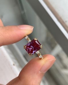 a person holding a ring with a red stone in it's middle and two white diamonds on each side