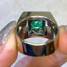 a person holding a ring with a green stone in it