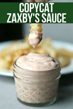 a person dipping some food into a small glass jar with the words copycat zaxby's sauce on it