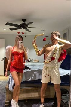 two people dressed in costumes standing next to each other near a bed with a ceiling fan