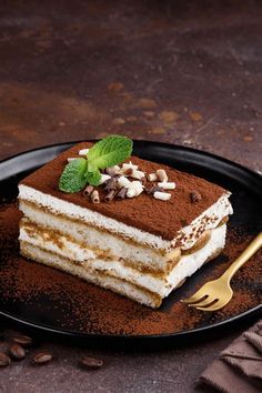 a piece of tirami cake on a black plate with a gold fork next to it