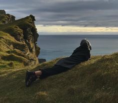 a person laying on top of a grass covered hill next to the ocean and cliffs