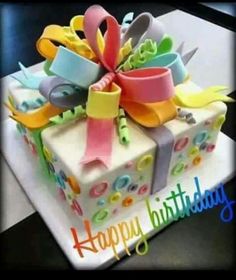 a birthday cake decorated with colorful ribbons and scissors on top of a white box that says happy birthday