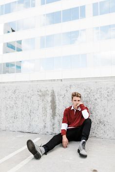 a young man sitting on the ground in front of a building