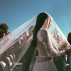 a woman in a wedding dress and veil walking down the aisle with people behind her