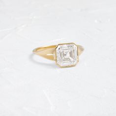 a gold ring with an emerald cut diamond in the center on a white tablecloth