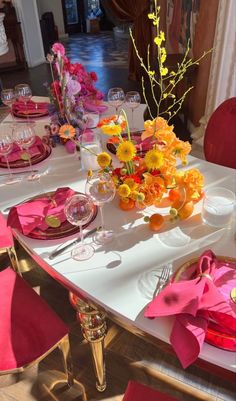 the table is set with pink and yellow plates, silverware, and colorful flowers