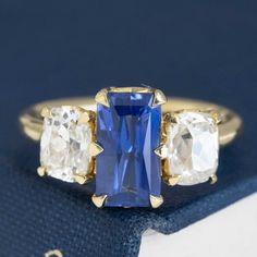 A JbyG trilogy ring with the most delicious sapphire we've come across in a while! That delicious royal blue velvety color in the center is irresistible, flanked by chunky, rustic elongated old mine cut diamonds. Together, they give you tons of color, sparkle, and spread across the top of one's finger. All set in yellow gold, this is one of our favorite original rings to come out of production as of late! 18kt yellow gold Size 6 and fully resizable Sapphire measures 9.87 x 5.53 x 3.75mm, heated Luxury Sapphire Ring With Three Stone Baguette Cut, Luxury Three-stone Sapphire Ring With Baguette Cut, Luxury Three Stone Sapphire Ring With Baguette Cut, Fine Jewelry Tanzanite Three Stone Sapphire Ring, Sapphire Three Stone Ring With Baguette Cut Diamonds, Fine Jewelry Three Stone Lab-created Sapphire Ring, Wedding Sapphire Ring With Three Stones In Radiant Cut, Fine Jewelry Three Stone Baguette Cut Sapphire Ring, Timeless Sapphire Three-stone Diamond Ring