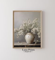 a white vase filled with flowers sitting on top of a wooden table next to a wall