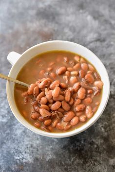 a white bowl filled with beans on top of a gray counter next to a spoon