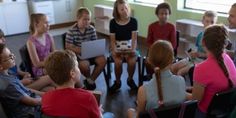 a group of children sitting in chairs around each other with laptops on their laps