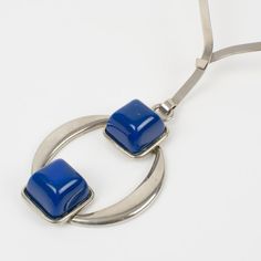 This is part of Chairish’s Costume Jewelry assortment.  Stylish Mid Century Modern Space Age collar necklace with a geometric pendant. A stainless steel rigid neckband and a pendant ornate with dimensional cobalt blue resin cabochons. No visible maker's mark. Measurements: neckband circumference is 15.38 in (39 cm) - pendant is 3.38 in long (8.5 cm) x 2.38 in wide (6 cm).  Please see the measurements noted above in the description for the best approximate dimensions. Modern Blue Metal Necklace, Luxury Modernist Necklace With Large Pendant, Mid-century Silver Necklace Gift, Modernist Sterling Silver Necklace With Polished Finish, Vintage Nickel-free Enamel Necklaces, Geometric Pendant, Maker's Mark, Space Age, Modern Spaces