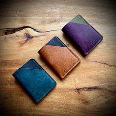 three different colored leather wallets sitting on top of a wooden table