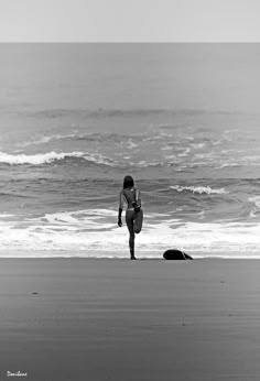 a woman standing on top of a beach next to the ocean holding a surfboard