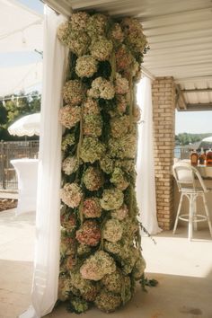 flowers are growing on the side of a white structure with curtains in front of it