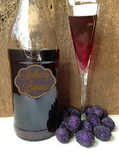 a bottle of mulberry liquor next to some purple berries and a glass of wine