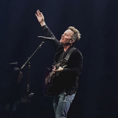 a man with his hand in the air while playing an acoustic guitar and singing into a microphone