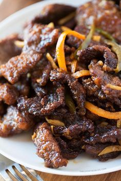 a white plate topped with meat covered in gravy and orange peels next to a fork