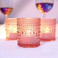 three pink glass cups sitting on top of a table next to two wineglasses