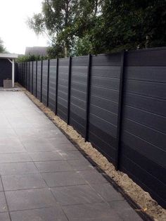 a long black fence is next to a paved area in the back yard with trees