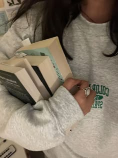 a woman is holding several books in her hands and wearing a ring on her left hand