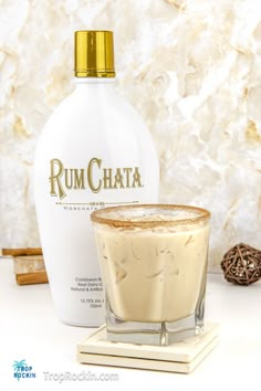 a bottle of rumchata next to a glass filled with liquid and cinnamon sticks