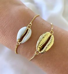 Features genuine Cowrie Shells, dipped in gold plating and affixed to a 14k gold filled box style chain. The bracelet is fully adjustable for a customized fit. Simply slide the gripper disc to your liking. It holds securely. Choose from White with gold trim or All gold. (Bamboo Cuff bracelet shown layered is available separately in the shop) Makes a great gift! I have Cowrie Necklaces available in the shop as well, so take a look around! *Please avoid showering, swimming or spraying perfume with Resizable Gold Jewelry As A Gift, Gift 14k Gold Filled Bracelets With Adjustable Chain, Trendy Adjustable Jewelry As A Gift For Her, Gift Bracelets With Adjustable Chain In 14k Gold Filled, Adjustable Gold Plated Jewelry For Gift, Adjustable Gold-plated Jewelry For Gifts, Trendy Resizable Gold Jewelry, Dainty Gold Bracelets For Beach, 14k Gold Filled Jewelry For Friendship