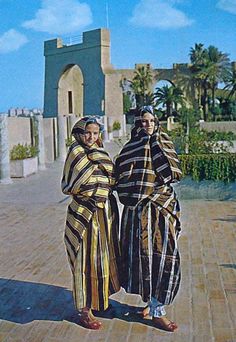 two women dressed in striped clothing standing next to each other on a brick walkway with palm trees behind them