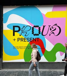 two women walking past a colorful advertisement on the side of a building