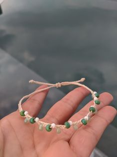 a hand holding a string bracelet with green and white beads